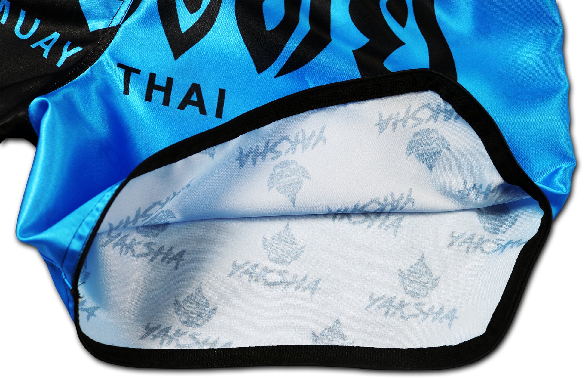 Inside view of two tone Muay Thai shorts in black and blue showing white inner lining with repeating YAKSHA logo print, handcrafted in Thailand.