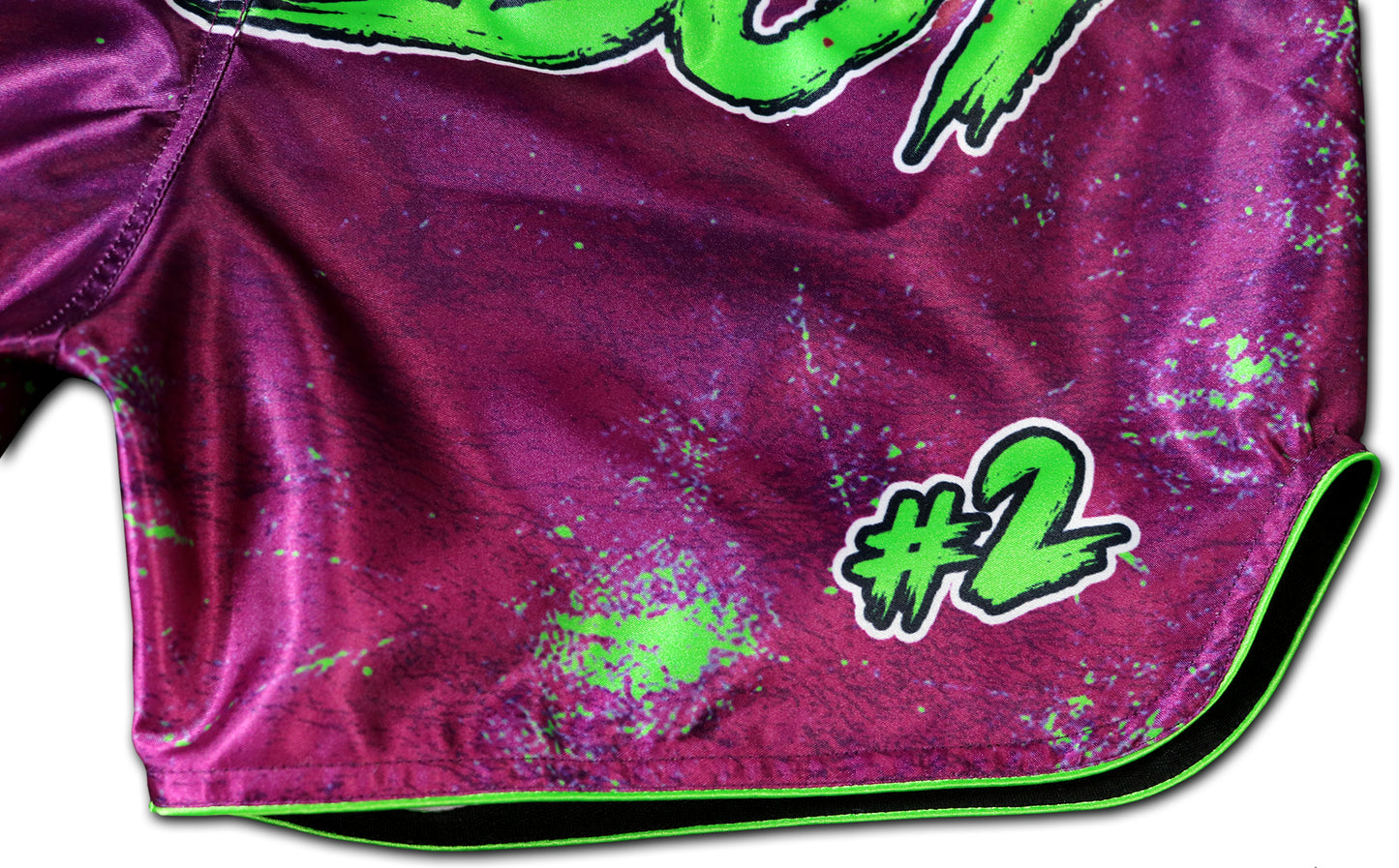 Detail of the front leg on Wild Boy Muay Thai Shorts showing shiny purple satin fabric, neon green paint splatter design, bold #2 graphic, neon green trim, handmade in Thailand, extreme limited edition, customizable with name.