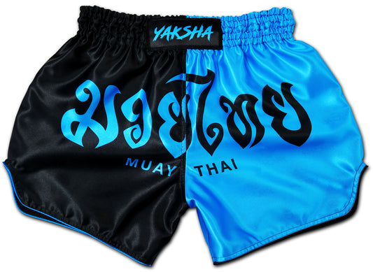 Two tone Muay Thai shorts in black and blue with YAKSHA logo and Thai lettering, handcrafted satin fight shorts made in Thailand.