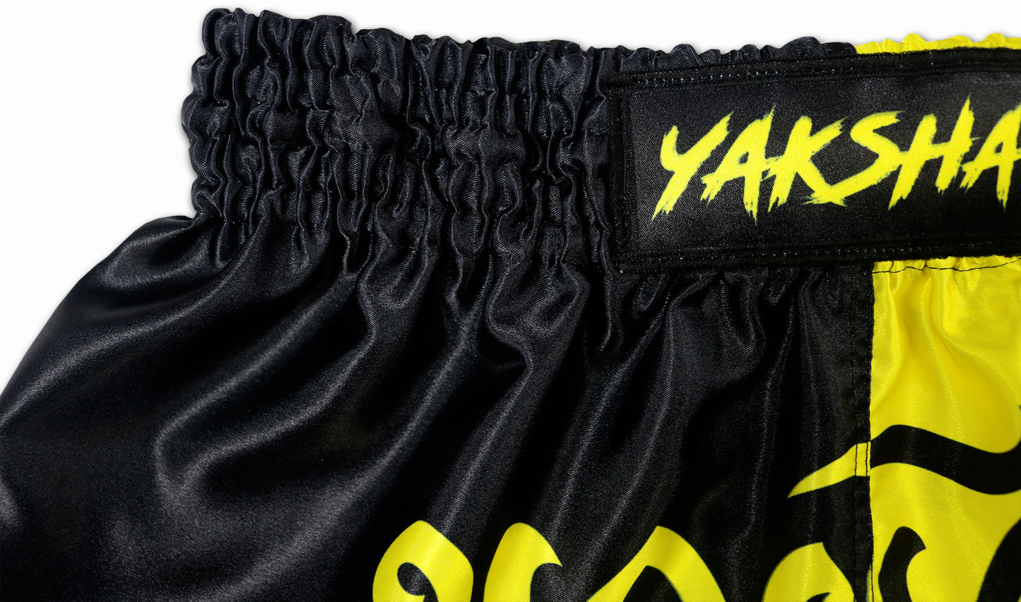 Close-up of the YAKSHA Luk Krung Muay Thai Shorts waistband with yellow YAKSHA brand logo on black elastic waistband