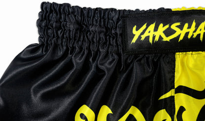 Close-up of the YAKSHA Luk Krung Muay Thai Shorts waistband with yellow YAKSHA brand logo on black elastic waistband