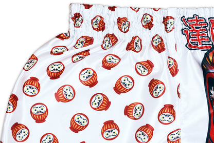 Detail of fierce daruma face graphic with blue waves, golden kanji and red trim on white Japan-inspired training shorts
