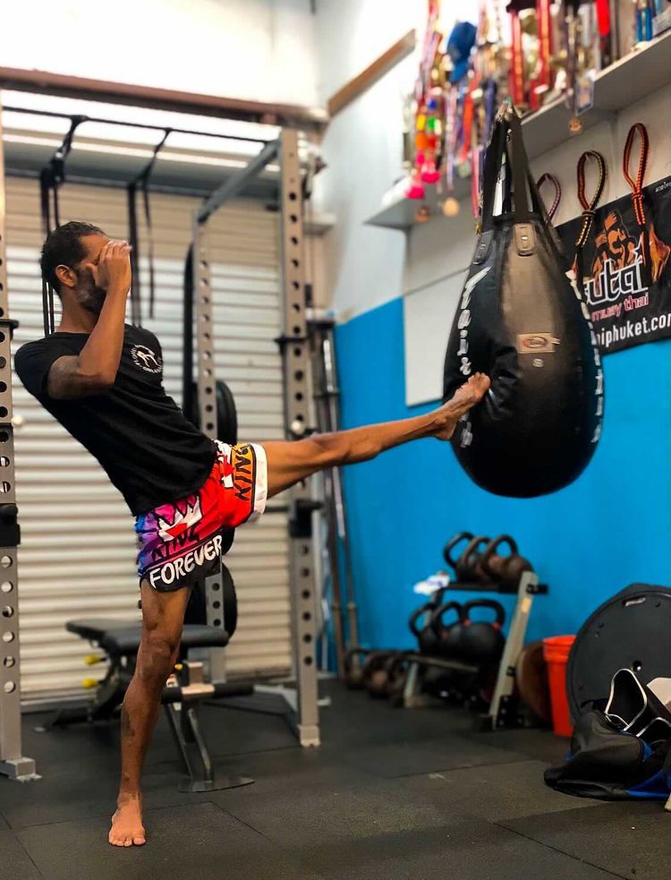 Fighter throwing high kick at heavy bag wearing red KING Forever Pride Boxing Trunks during Muay Thai training