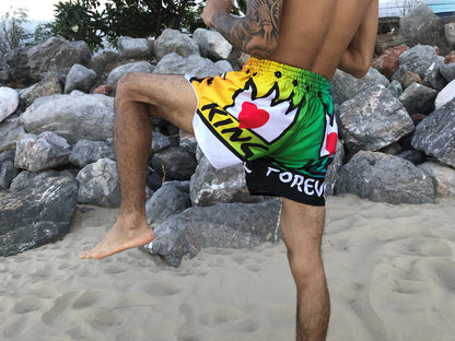 Tattooed fighter in green KING Forever Pride Boxing Trunks performing knee strike on the beach in Thailand