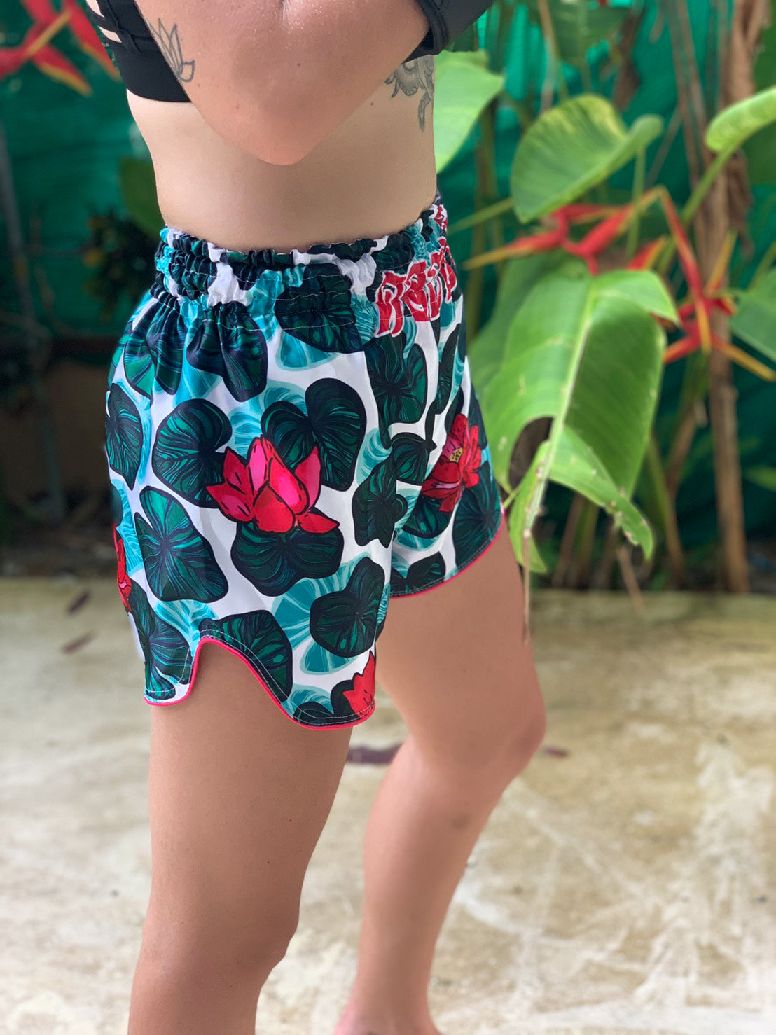 Woman wearing Lotus Flower Muay Thai Shorts with pink lotus blossoms and tropical lily pad pattern outdoors