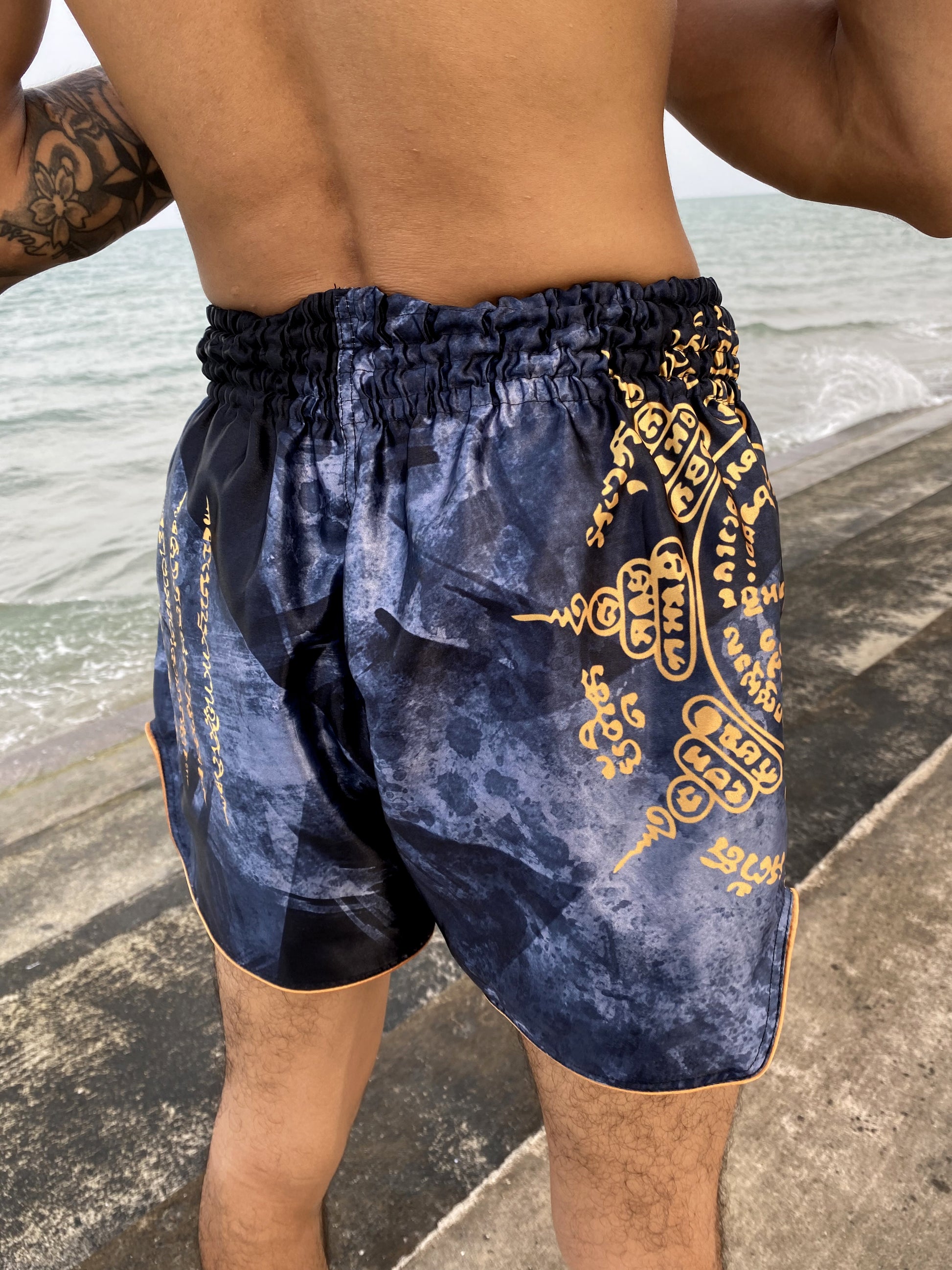 Back view of Phaya Naga Muay Thai fight shorts in black showing gold Sak Yant sacred Thai script on the hip and golden piping
