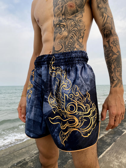 Fighter wearing Phaya Naga Muay Thai fight shorts in black at the beach, gold Naga head with flames printed on the side