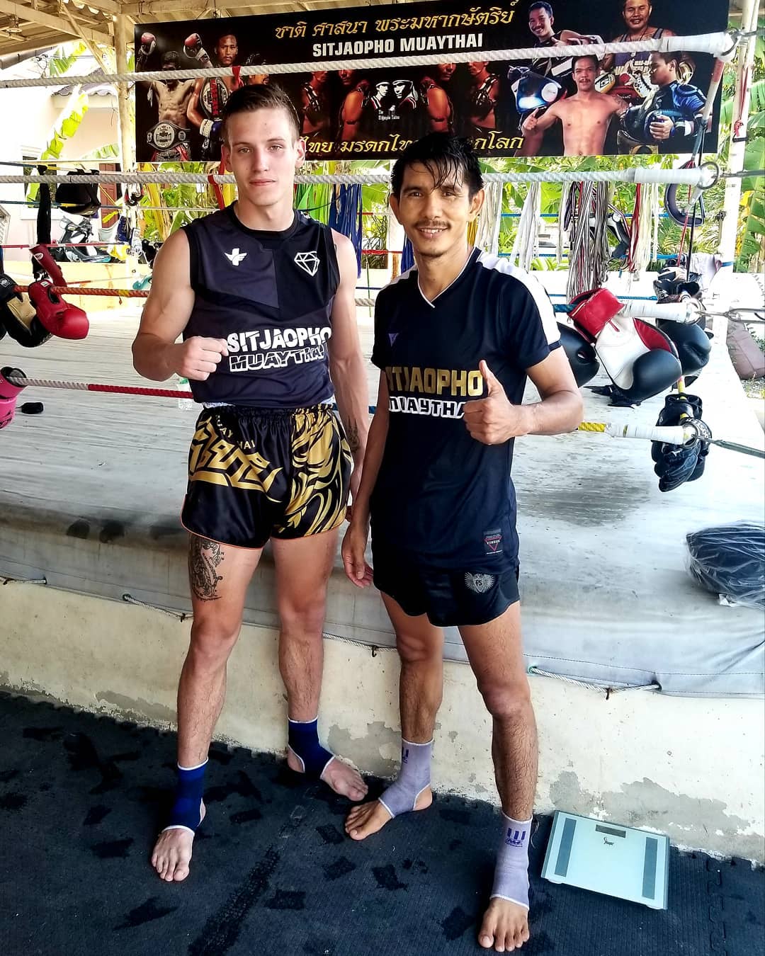 Tribal Samurai Muay Thai Boxhose Schwarz Gold getragen von einem Kunden beim Muay Thai Training neben einem thailändischen Trainer im Sitjaopho Muay Thai Camp in Thailand