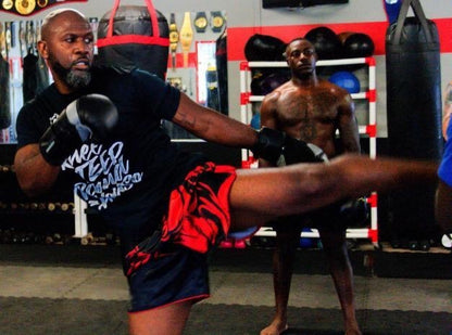A customer who bought this shorts  throwing a powerful high roundhouse kick wearing black and red Tribal Samurai boxing shorts during heavy bag training
