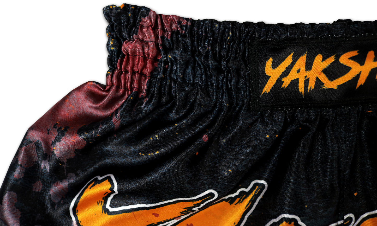 Close up of red satin waistband bleed and YAKSHA logo tape on the Grunge Black Orange shorts