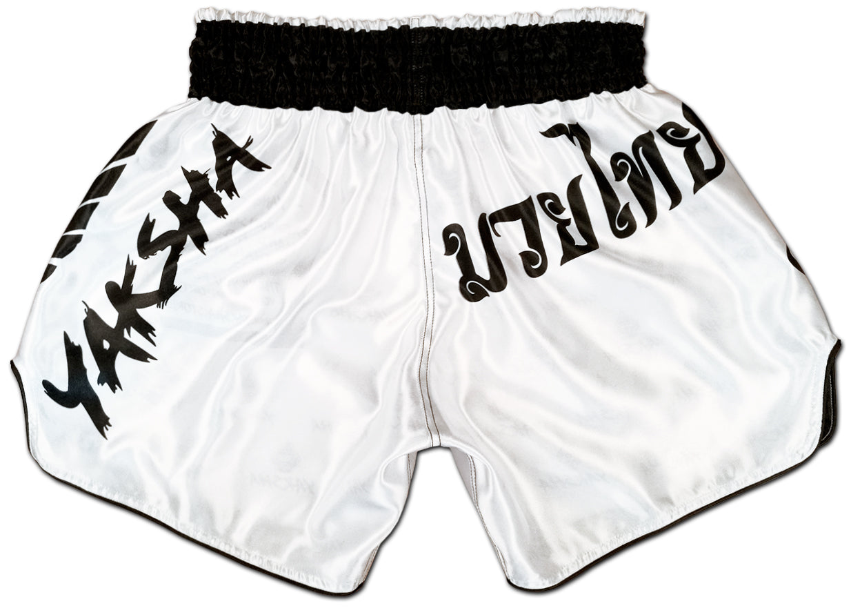 YAKSHA Yin and Yang training shorts back view, clean white satin with YAKSHA script, Thai lettering and black satin piping on all edges