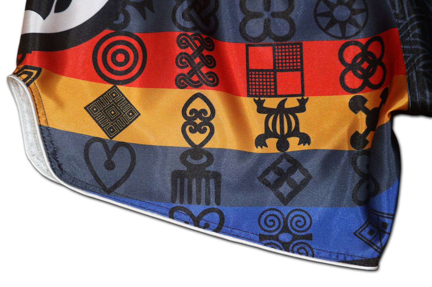 Close up of glossy satin fabric and red blue gold Adinkra symbol stripes on BLACK PANTHER Muay Thai fight shorts