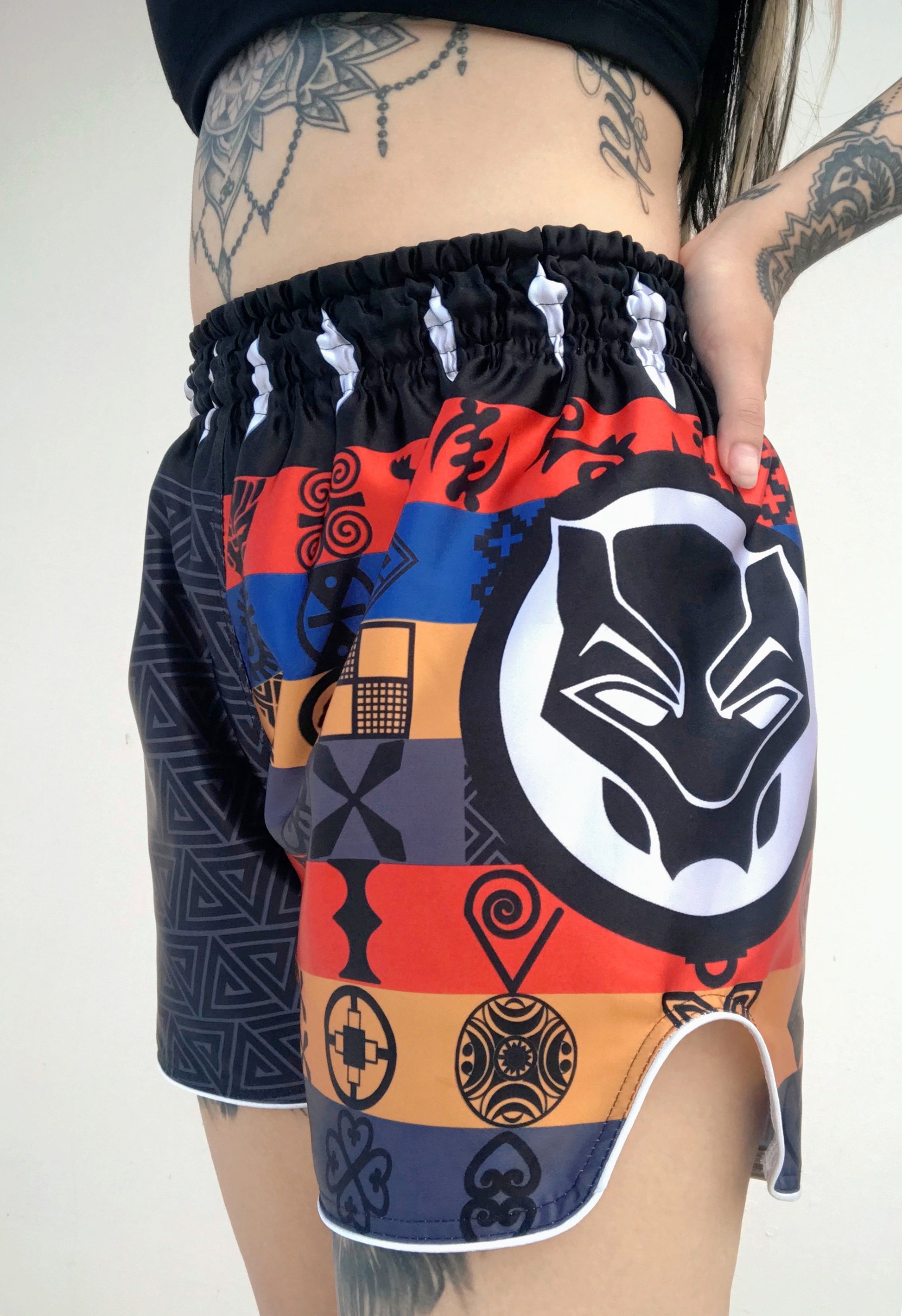 Woman wearing BLACK PANTHER Adinkra Muay Thai fight shorts during training with visible side slit and panther logo