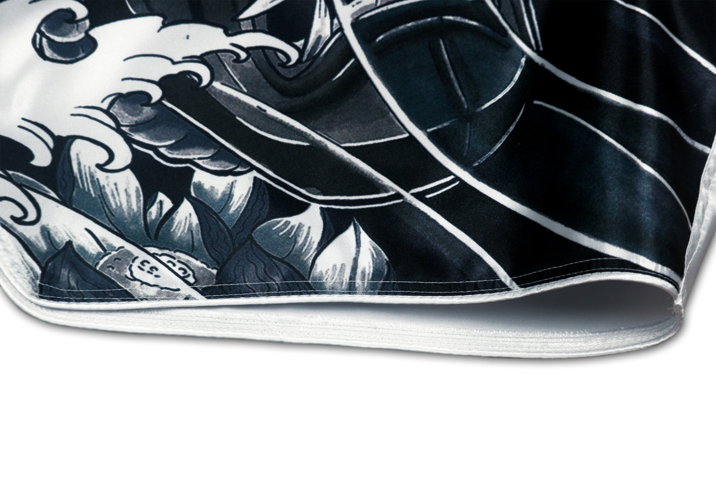 Detail of the Cherry Blossom Samurai shorts showing the black and grey hannya mask, traditional Japanese wave pattern and white satin piping along the bottom edge