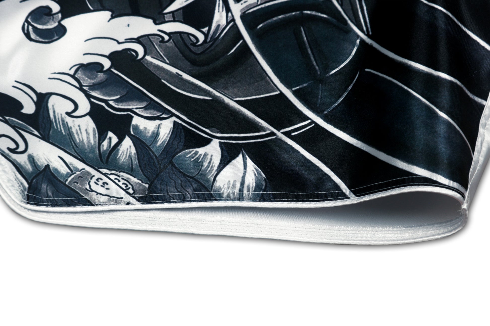 Detail of the Cherry Blossom Samurai shorts showing the black and grey hannya mask, traditional Japanese wave pattern and white satin piping along the bottom edge