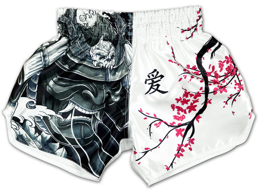 Front view of Cherry Blossom Samurai Muay Thai Boxing Shorts on white satin with a black hannya mask and dark wave artwork on the left panel and pink cherry blossom branches on the right panel
