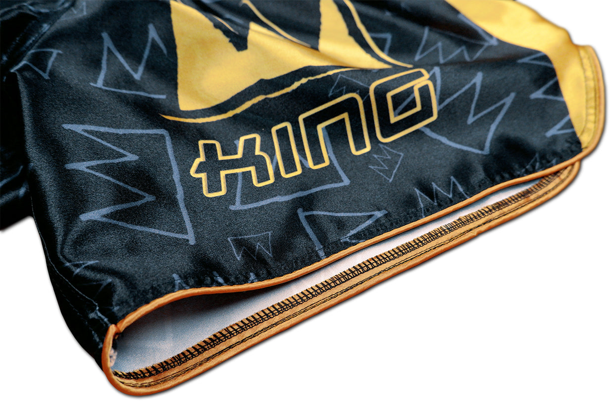 Detail of stitched KING lettering, gold hem and crown graffiti pattern on black satin Thai fightwear