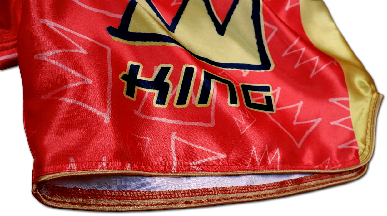 Detail of stitched KING crown logo, gold hem and crown graffiti pattern on red satin Thai fightwear