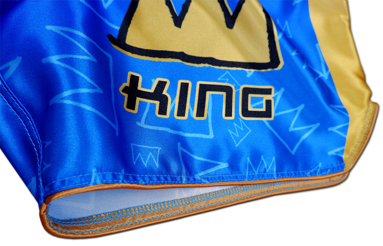 Detail of KING lettering, gold hem stitching and crown graffiti pattern on royal blue satin Thai fightwear
