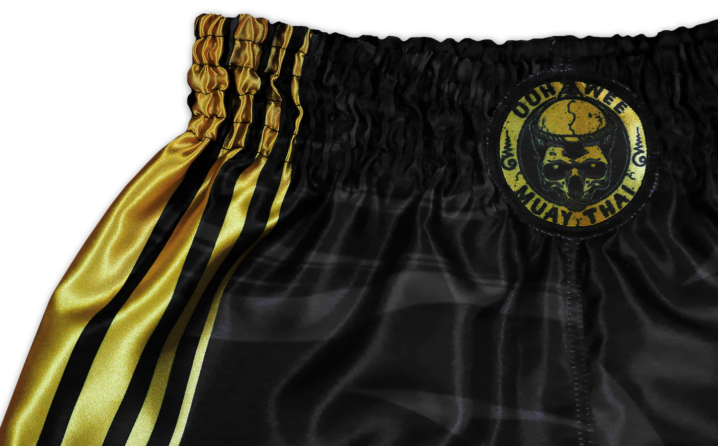 Kickboxing Shorts detail showing the iconic OOWEE Muay Thai skull logo and gold stripes on black satin