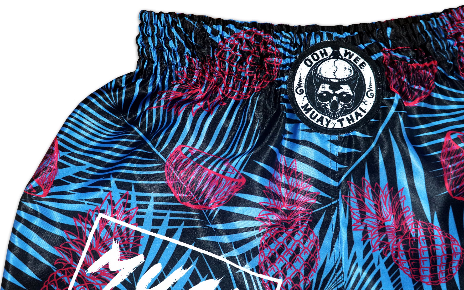 OOWEE Tropical Thai Boxing Shorts detail showing the iconic OOWEE Muay Thai skull logo on black blue and pink satin