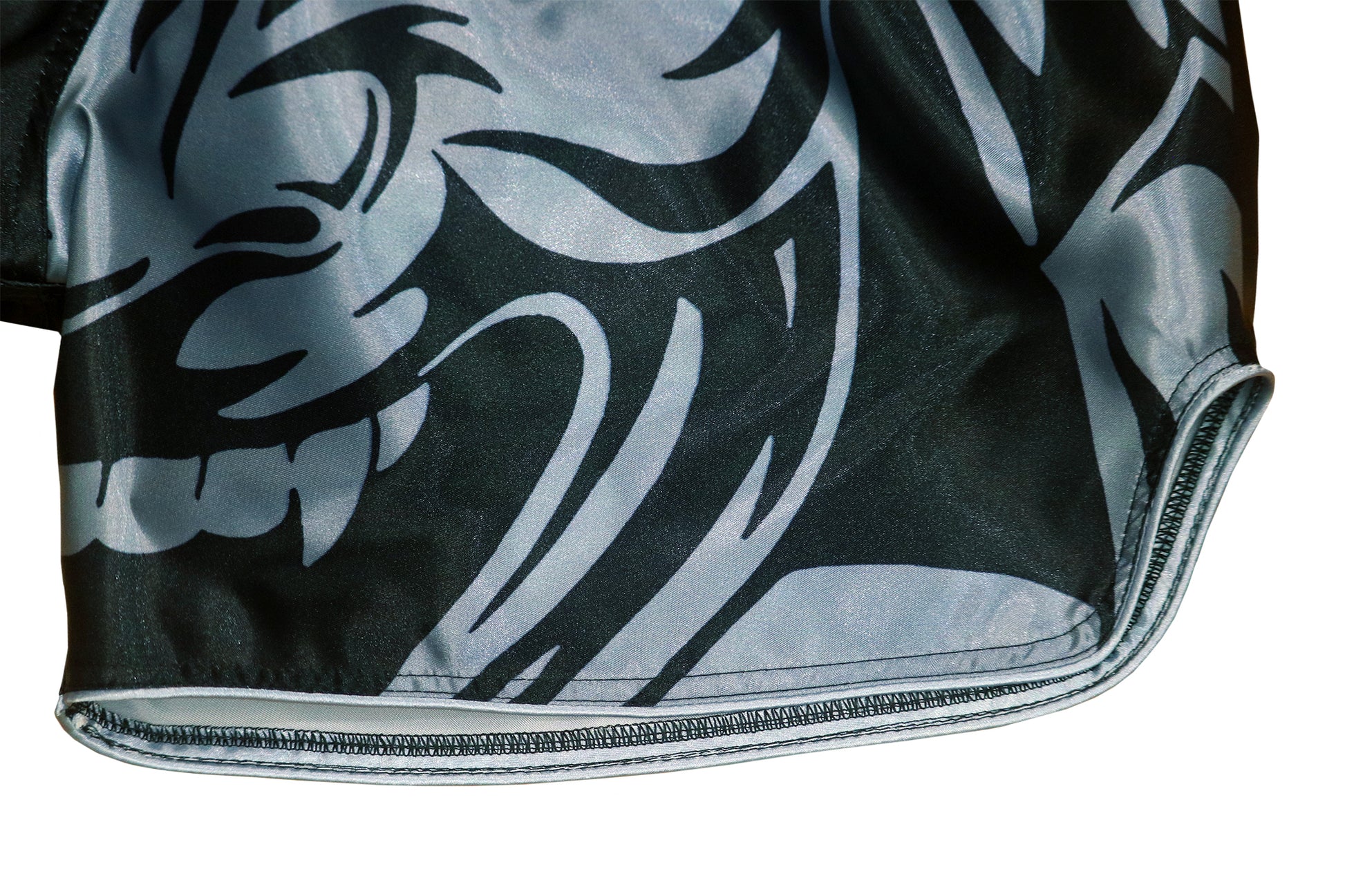 Detail of fierce tribal samurai mask graphic with sharp silver gray and black lines and reinforced hem on Thai fight shorts