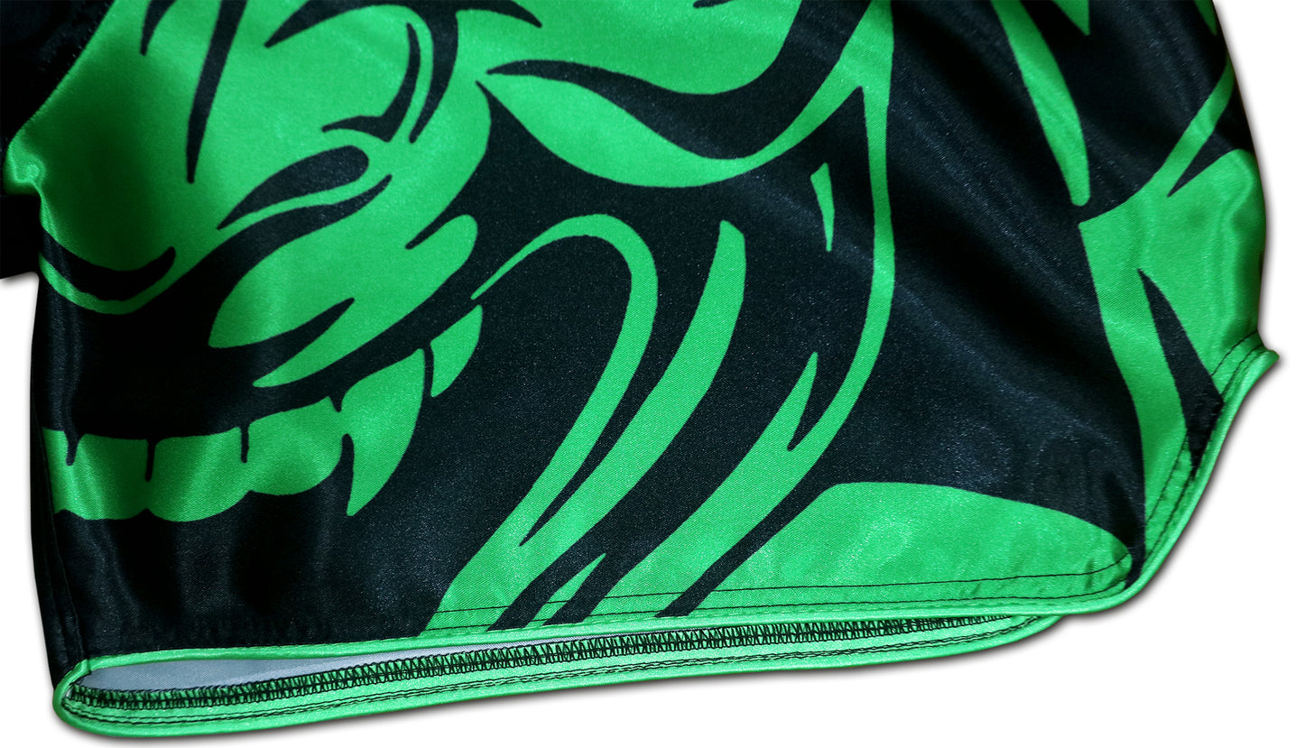 Detail of fierce tribal samurai mask graphic with sharp green and black lines and reinforced hem on Thai fight shorts