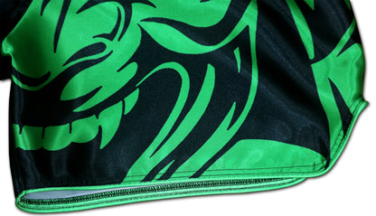 Detail of fierce tribal samurai mask graphic with sharp green and black lines and reinforced hem on Thai fight shorts
