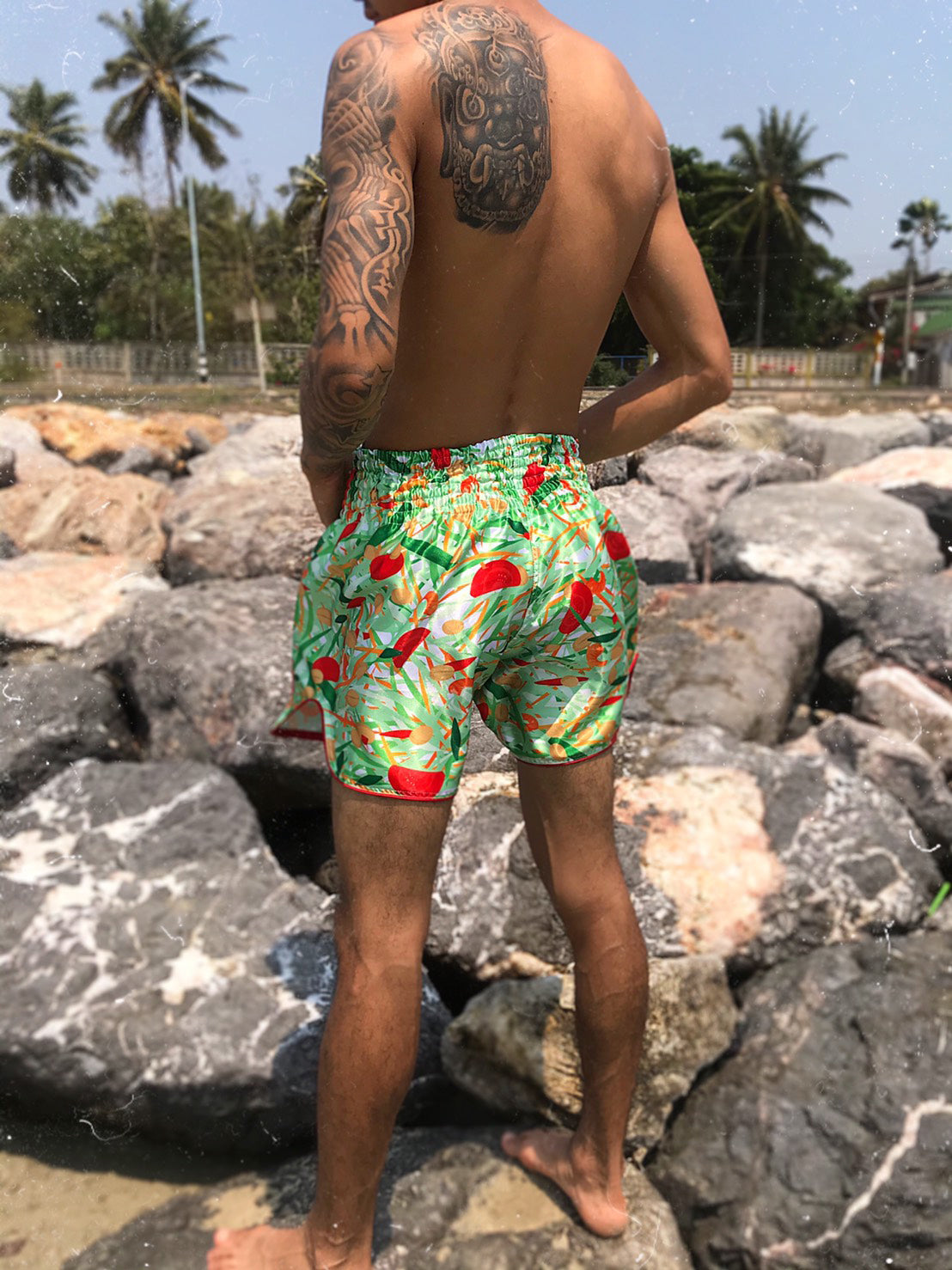 Back view of Thai boxer wearing SOM TAM Muay Thai Shorts on rocky coastline in Thailand