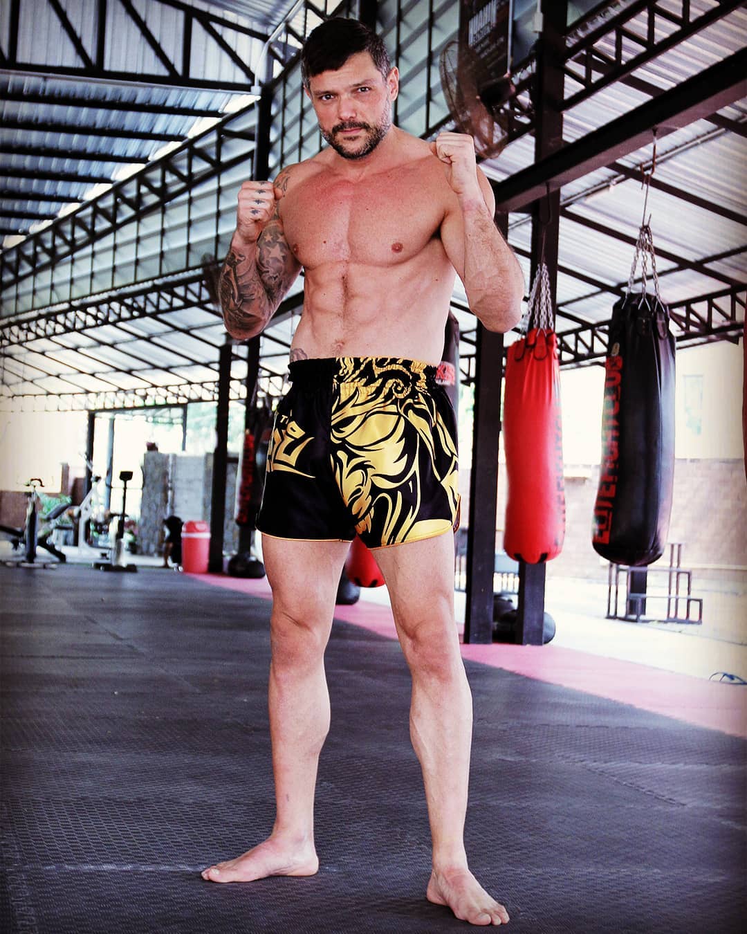 Tribal Samurai Muay Thai Boxing Shorts Black Gold close up on fighter training at a Muay Thai gym with heavy bags in the background
