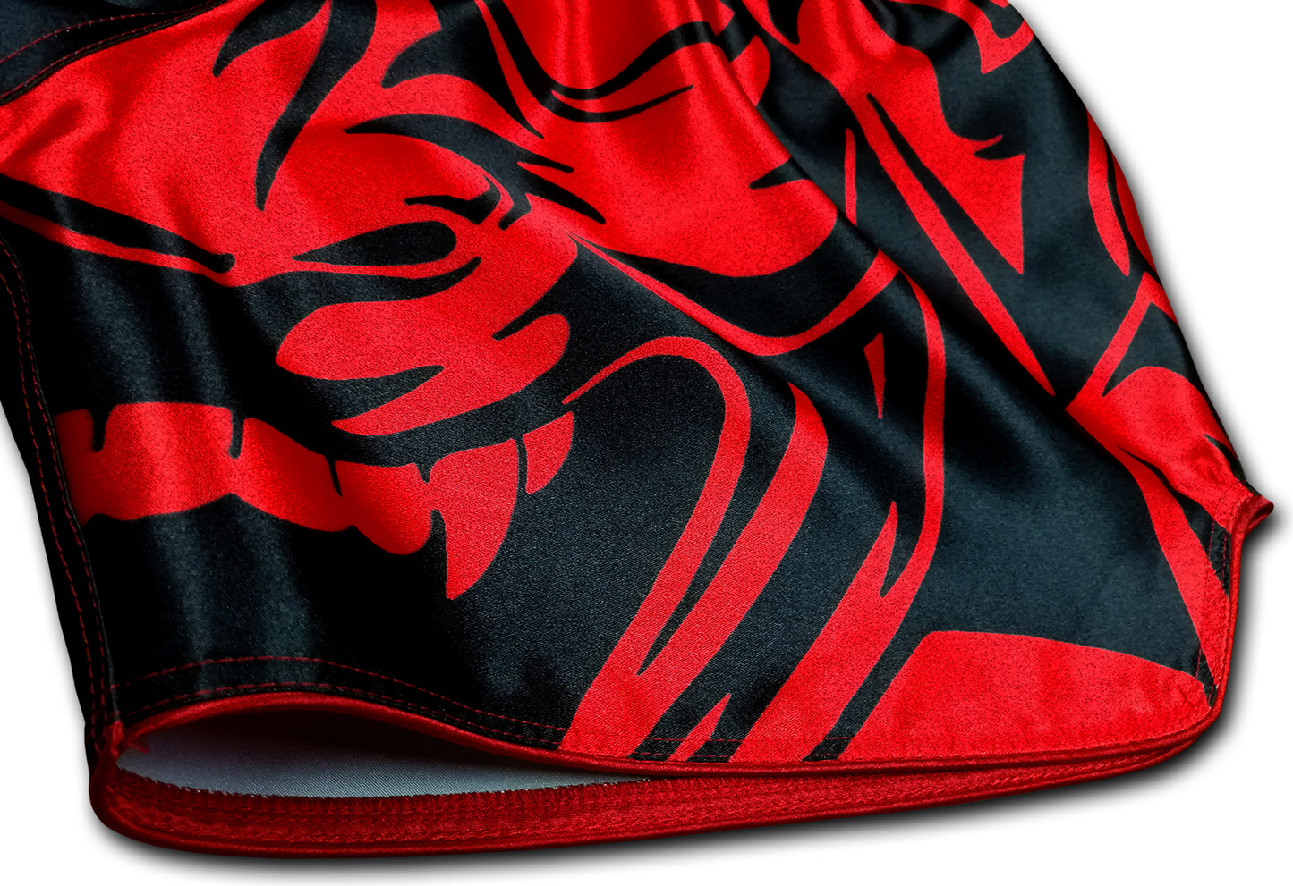 Close up detail of blood red oni demon face with sharp fangs and tribal patterns printed on smooth black satin Muay Thai boxing shorts
