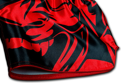 Close up detail of blood red oni demon face with sharp fangs and tribal patterns printed on smooth black satin Muay Thai boxing shorts