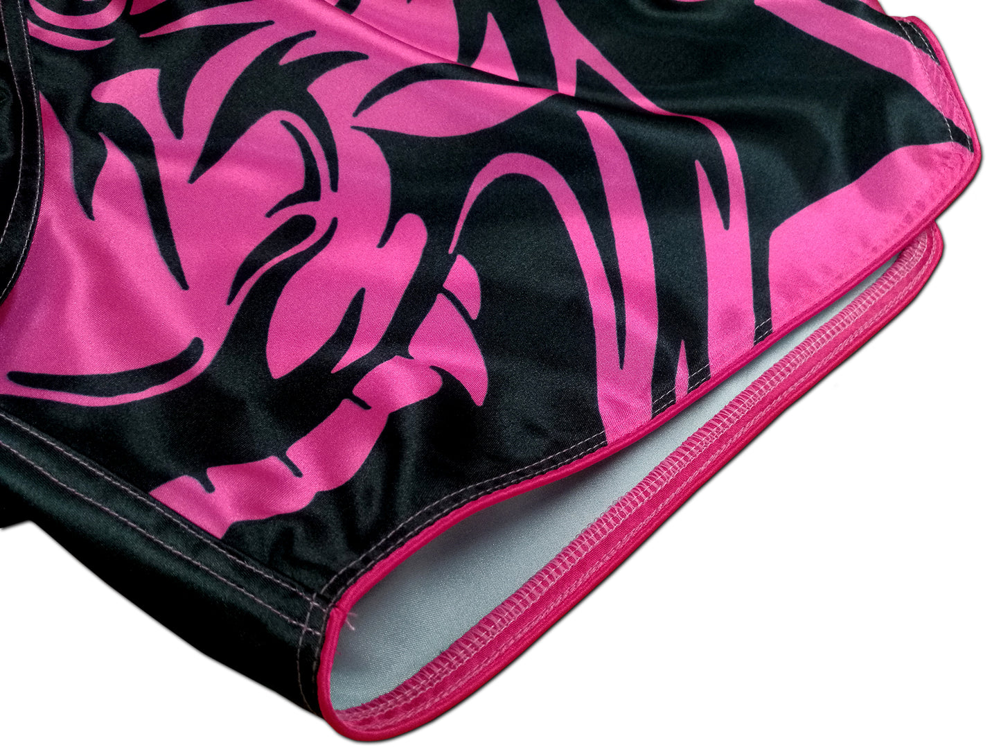 Detail of neon pink oni demon face with sharp fangs and tribal patterns printed on smooth black satin women's fight shorts
