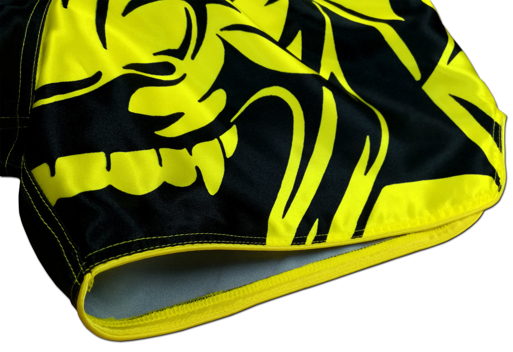 Detail of yellow oni demon face graphic with sharp fangs and tribal patterns printed on smooth black satin Thai fightwear