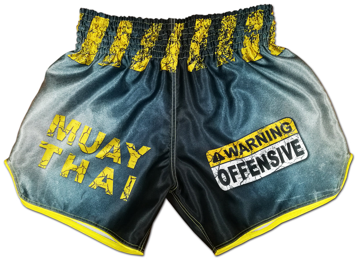 Gray and yellow Thai boxing shorts with cracked MUAY THAI lettering and WARNING OFFENSIVE tape graphic on the front